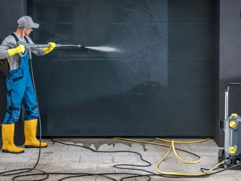 Homeowner cleaning white garage door with brush and soapy water for maintenance