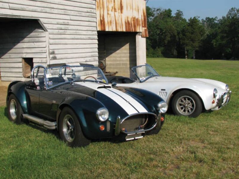 A sleek, silver 1966 Shelby Cobra 427 races on a track, showcasing its iconic curves and raw power