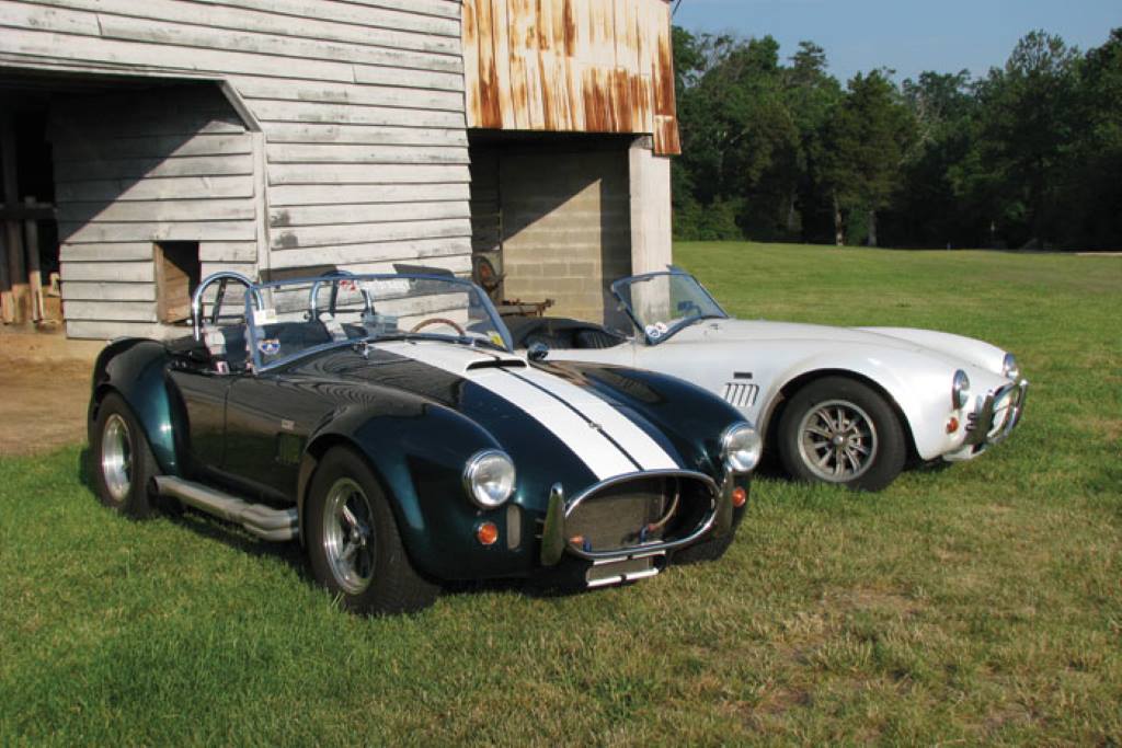 A sleek, silver 1966 Shelby Cobra 427 races on a track, showcasing its iconic curves and raw power