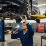 Mechanic inspecting car suspension and steering components under a lifted vehicle